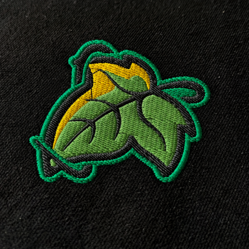 Close-up of a green and gold leaf embroidered on black fabric, showing the Elven Brooch T-shirt design.