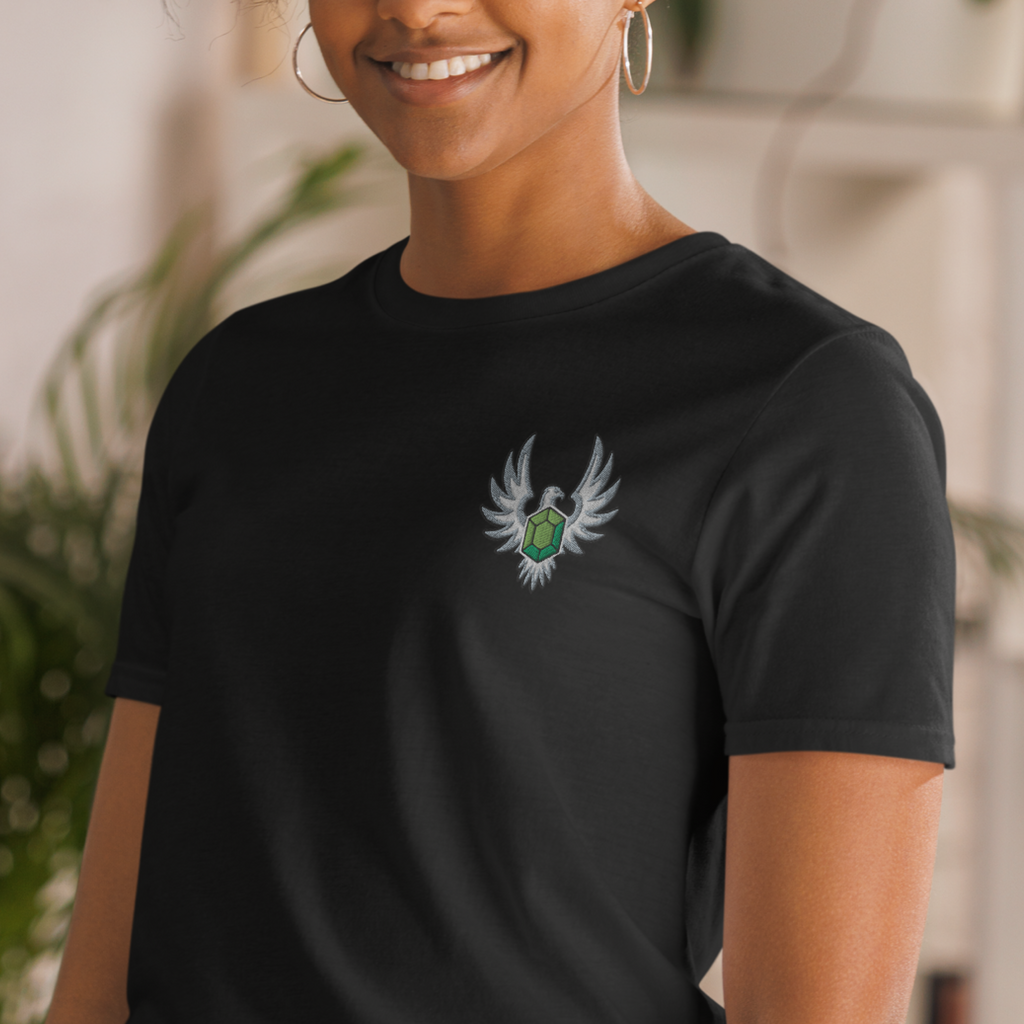 Model wearing a black Elven Stone T-shirt with a green gemstone framed by silver wings embroidered on the left chest.
