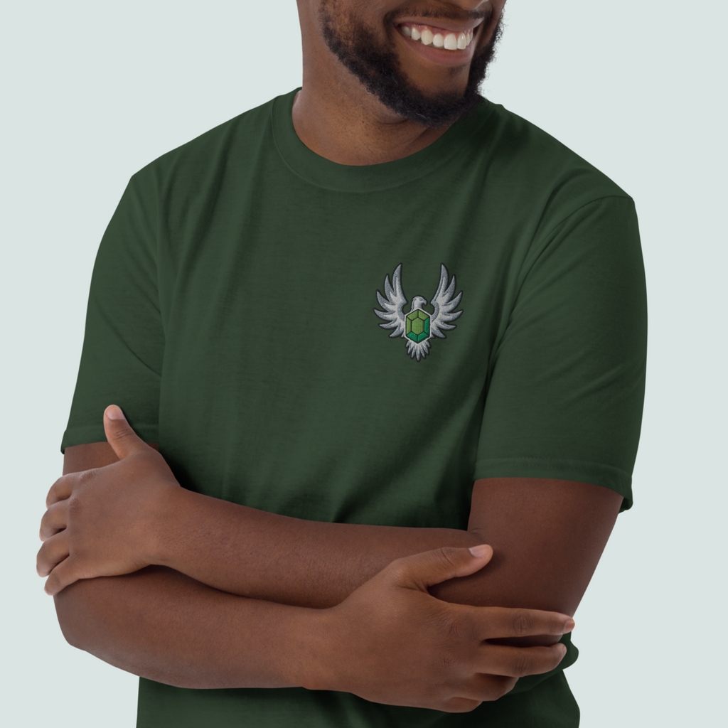 Model wearing a forest green Elven Stone T-shirt with a green gemstone framed by silver wings embroidered on the left chest.