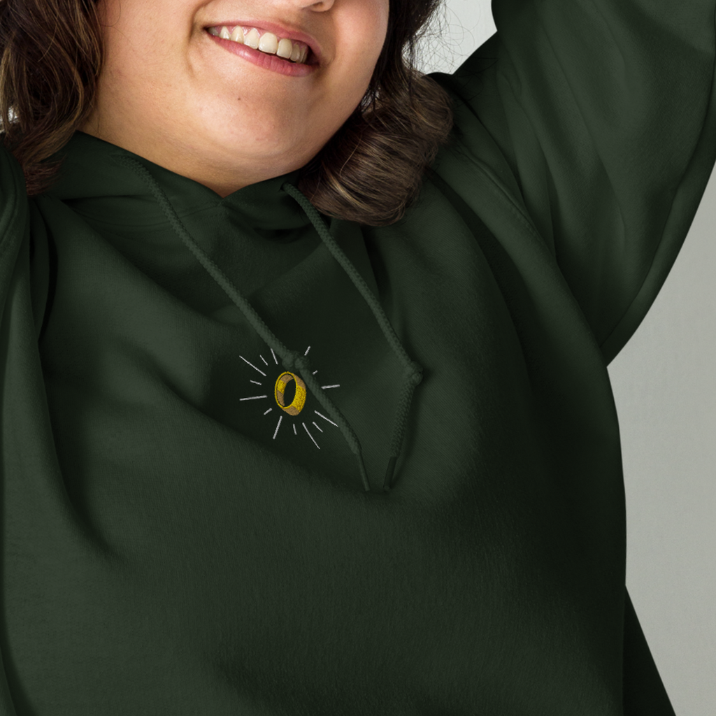 Model wearing a forest green The Master Ring hoodie with a gold ring surrounded by silver rays embroidered on the left chest.